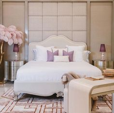 a large white bed sitting in a bedroom next to a tall pink flower vase on top of a table