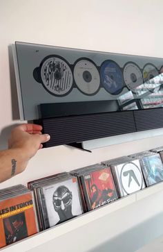 a person holding up a video game console with several cds on the shelf behind it