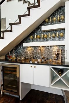 a kitchen under the stairs with wine bottles and glasses on it's counter top