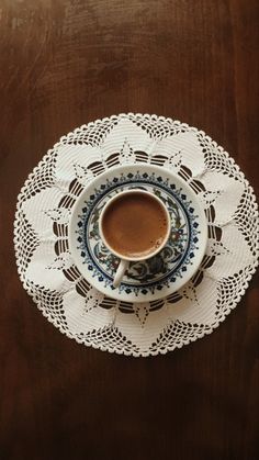 a cup of coffee sitting on top of a white doily next to a wooden table