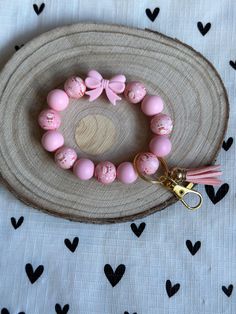 a pink and white beaded bracelet with tassels on a wooden plate next to a keychain