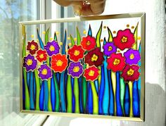 a person holding up a painting with flowers on it in front of a window sill