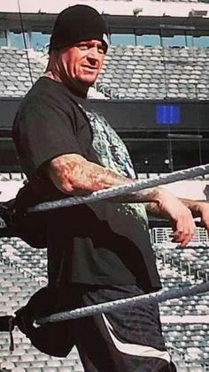 a man with tattoos on his arm holding a baseball bat in front of an empty stadium