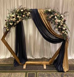 a gold and black wedding arch with flowers on the top, along with draping