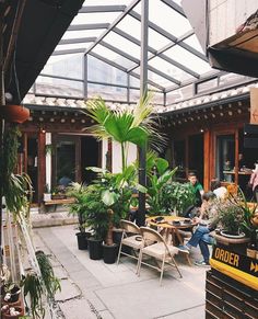 people are sitting at tables in an outdoor restaurant with plants and potted plants on the patio