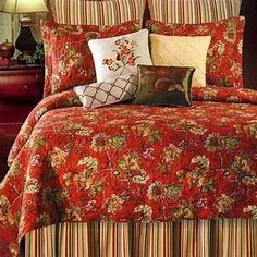 a bed covered in red and yellow floral bedspread with pillows on top of it