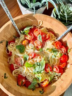 a wooden bowl filled with pasta and tomatoes