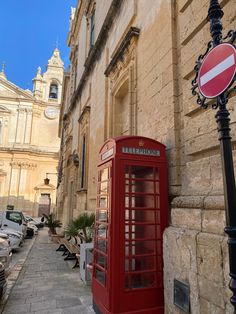 a red phone booth sitting on the side of a building next to a street sign