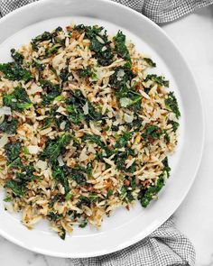 a white plate filled with rice and greens on top of a marble countertop next to a napkin