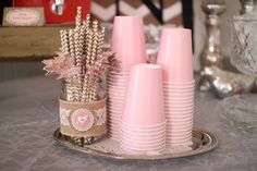 pink cups and straws are arranged on a silver tray in front of other decorative items