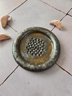 an old metal dish with holes in it on the floor next to garlic florets