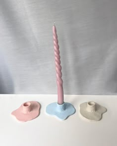 three different colored candles sitting on top of a white table next to eachother