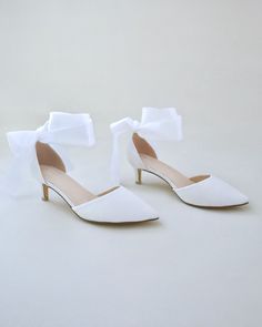 a pair of white high heeled shoes with a bow