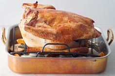 a roasting pan with a whole chicken in it's bottom half, on a white surface