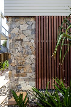 an outdoor shower in front of a house with wood slats on the side and stone walls