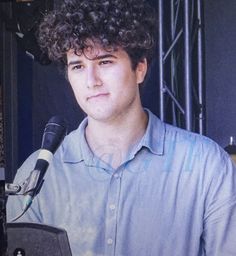 a man with curly hair sitting in front of a microphone and holding a laptop computer