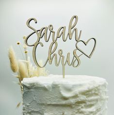 a white cake topped with a wooden name and two hearts on it's top