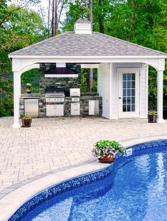 an outdoor kitchen next to a pool in the middle of a yard with a grill