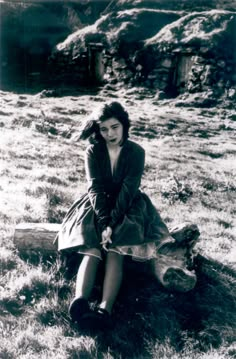 an old photo of a woman sitting on a log in the grass with her legs crossed