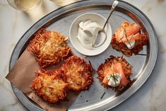 four crab cakes on a silver tray with a bowl of cream and two glasses of wine