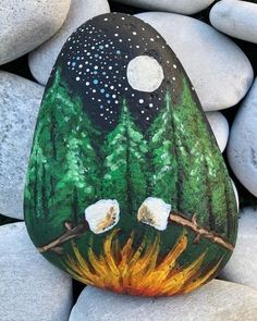 a painted rock sitting on top of a pile of rocks with trees and moon in the sky