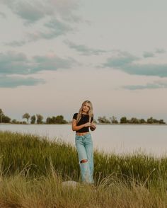 a woman standing in tall grass next to a body of water