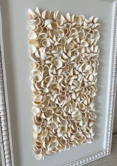 an art piece made out of seashells in a white frame on the wall