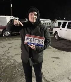 a man pointing at the camera while wearing a hoodie and holding a license plate