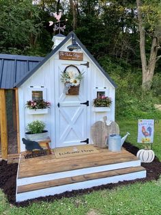 a small white shed with flowers and plants on the front porch, next to a sign that says garden news