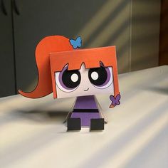 a paper doll with an orange hair and purple dress sitting on top of a table