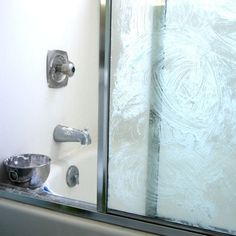 a glass shower door next to a bath tub and toilet paper dispenser