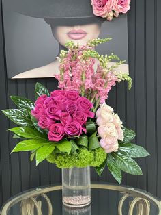 a vase filled with pink and green flowers on top of a glass table next to a black wall