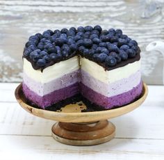 a cake with blueberries and cream on top is sitting on a wooden stand in front of a wood wall