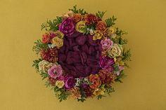 an arrangement of flowers arranged in a circle on a yellow background with green leaves and stems