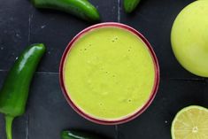 a green smoothie in a red bowl next to sliced limes and jalapenos