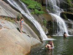 three people are in the water near a waterfall