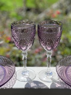 two wine glasses sitting next to each other on a window sill with flowers in the background