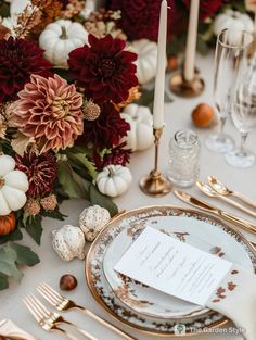 the table is set with gold and white plates, silverware, candles, and flowers