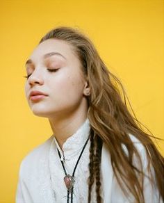 a woman with long hair wearing a white shirt and braids standing in front of a yellow wall