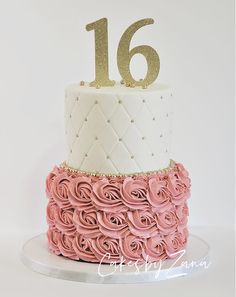 a white and pink cake with gold number 16 on top, sitting on a plate