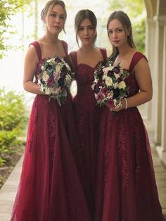 three women in long dresses standing next to each other on a porch with greenery