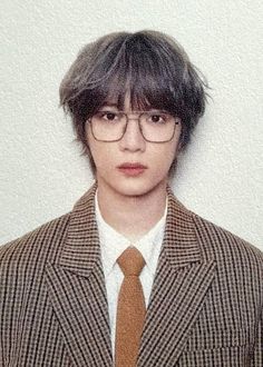 a young man wearing glasses and a suit with a brown tie is standing in front of a white wall