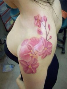 a woman's breast with pink flowers painted on her chest and shoulder, in the process of being tattooed