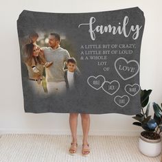 a woman holding up a blanket with the words family and two hearts on it, in front of a white wall