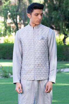 Grey nehru jacket with floral thread, cutdana embroidery and concealed placket. Paired with embroidered kurta and a plain pyjama.
Components: 3
Pattern: Embroidered
Type Of Work: Thread
Neckline: Mandarin collar
Sleeve Type: Kurta: Full, Jacket: Sleeveless
Fabric: Russian Silk, Pure Silk
Color: Grey
Other Details: 
Concealed placket
Side slits
Note: The pocket square worn by the model is not for sale
Occasion: Wedding - Aza Fashions Designer Nehru Jacket With Chikankari Embroidery And Stand Collar, Festive Designer Nehru Jacket With Stand Collar, Long Sleeve Embroidered Nehru Jacket For Reception, Embroidered Long Sleeve Nehru Jacket For Reception, Designer Nehru Jacket With Chikankari Embroidery For Eid, Designer Nehru Jacket With Chikankari For Eid, Festive Bandhgala With Chikankari Embroidery And Stand Collar, Designer Nehru Jacket With Mirror Work For Reception, Formal Nehru Jacket With Resham Embroidery And Stand Collar