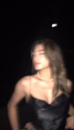 a blurry photo of a woman in a black dress at night with her hands on her hips