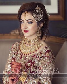 a woman in a red and gold bridal outfit with jewelry on her head, posing for the camera