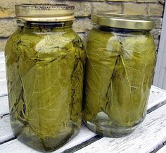 two jars filled with green leaves sitting on top of a wooden table