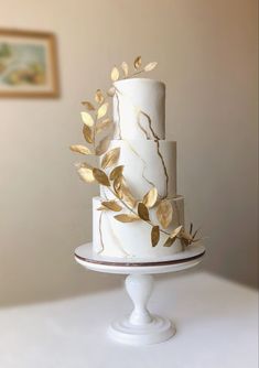 a three tiered white cake with gold leaves on top