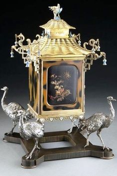 an ornate clock with two birds standing on it's legs and one bird sitting on top of the clock